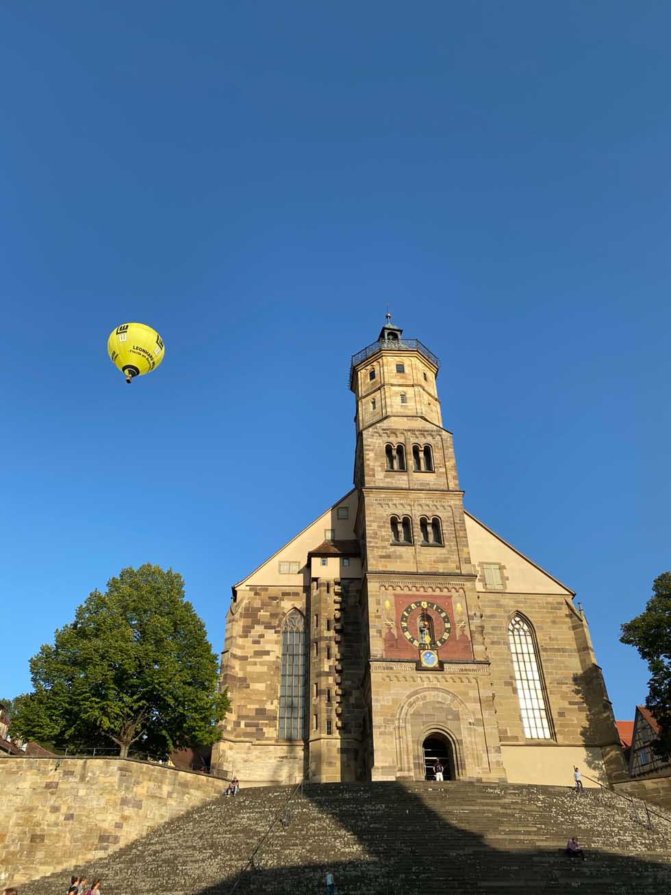 Historische Kirche St. Michael's in Schwäbisch Hall mit großer Treppe unter blauem Himmel mit Heißluftballon und beliebtes Ausflugsziel in der Region.