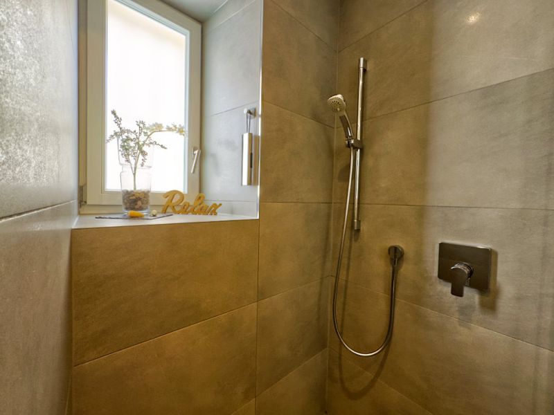 Stilvolle Dusche der Ferienwohnung mit bodengleicher Glasdusche, modernen Armaturen und Tageslichtfenster im modernen Design.