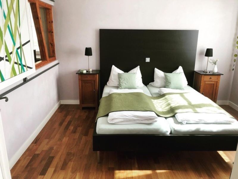 Helles Schlafzimmer der Ferienwohnung mit großem Doppelbett, Nachttischen und modernem Design in ruhiger Atmosphäre.