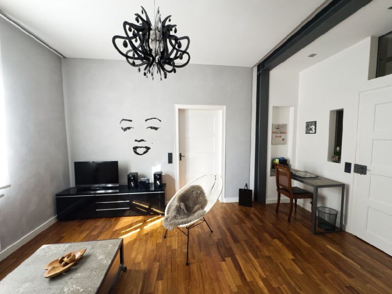 Großzügiger Wohnbereich der Ferienwohnung mit modernem Fernseher, stilvollem Kronleuchter, hochwertigem Parkettboden und kleinem Schreibtisch im offenen Altbau-Ambiente.